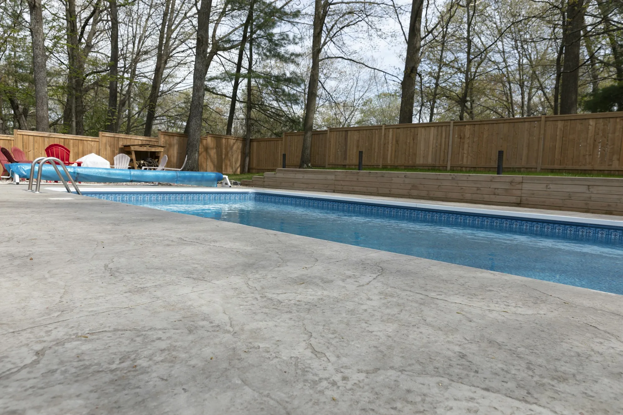Concrete pool deck beside an in-ground pool and wood fence